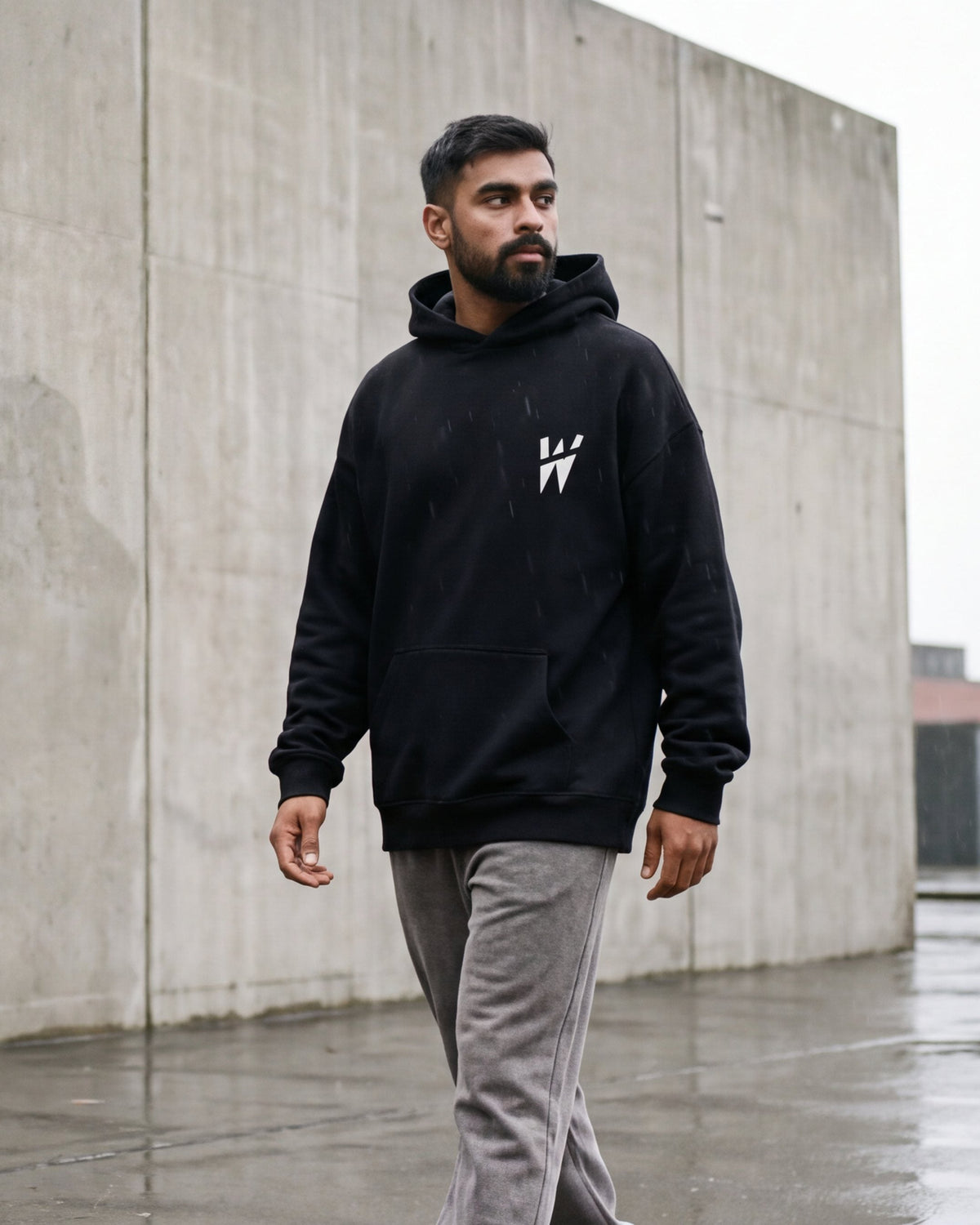 A man crossing a wet concrete rooftop in the WAYSHNER hoodie